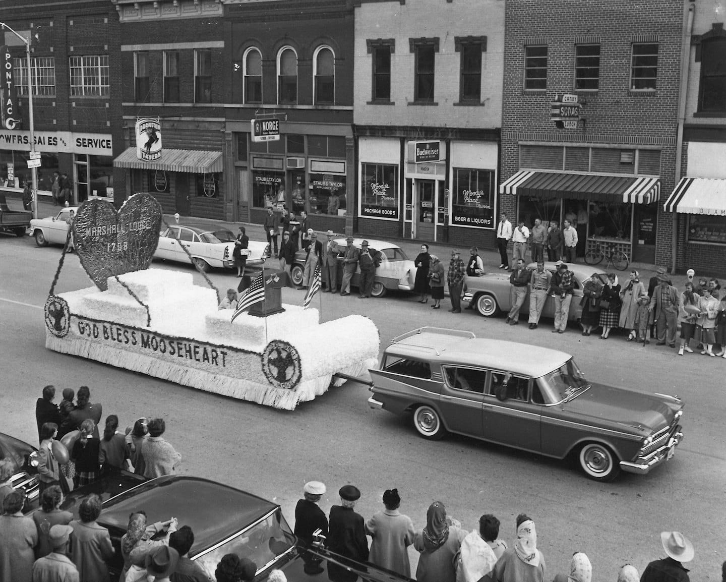 A vintage parade float pulls down a busy town street.